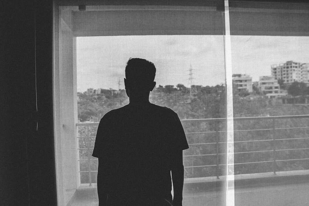 Silhouette of a man standing before a large window seen from behind